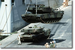 tanks with woodland camouflage being lowered from a ship